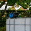 cuve-ibc-blanc-avec-pompe-220V-1000L-nettoye-palette-acier-plastique-vue-de-devant-dans-environnement-de-jardin.webp
