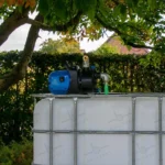 cuve-ibc-blanc-avec-pompe-220V-1000L-nettoye-palette-acier-plastique-vue-de-devant-dans-environnement-de-jardin.webp