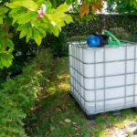 cuve-ibc-blanc-avec-pompe-220V-1000L-nettoye-palette-acier-plastique-vue-du-cote-gauche-dans-environnement-de-jardin.webp
