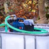 cuve-ibc-blanc-pompe-sur-batterie-1000L-nettoye-palette-acier-plastique-vue-de-droite-devant-avec-tuyau.webp