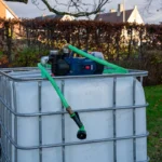 cuve-ibc-blanc-pompe-sur-batterie-1000L-nettoye-palette-acier-plastique-vue-de-gauche-environnement-du-jardin-avec-tuyau.webp