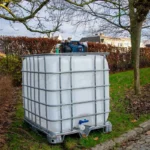 cuve-ibc-blanc-pompe-sur-batterie-1000L-nettoye-palette-acier-plastique-vue-de-gauche-environnement-du-jardin-sans-tuyau.webp