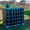 cuve-ibc-noir-avec-pompe-220V-1000L-renouvele-palette-acier-plastique-zijaanzicht-met-uitgaande-slang-in-tuinomgeving.webp