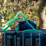 cuve-ibc-noir-avec-pompe-sur-batterie-1000L-renouvele-palette-acier-plastique-vue-de-cote-arrieere-avec-tuyau-sortant.webp