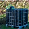 cuve-ibc-noir-avec-pompe-sur-batterie-1000L-renouvele-palette-acier-plastique-vue-de-cote-arrieere-avec-tuyau-sortant-dans-environnement-de-jardin.webp