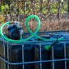 cuve-ibc-noir-avec-pompe-sur-batterie-1000L-renouvele-palette-acier-plastique-vue-de-cote-avec-tuyau-sortant.webp